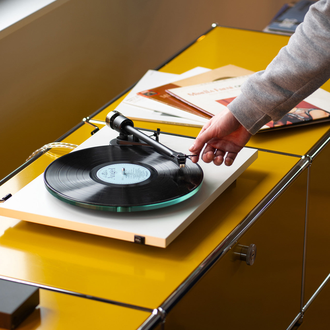 Lifestyle angled view of the Pro-Ject T2 Turntable in White, hand moving the tonearm